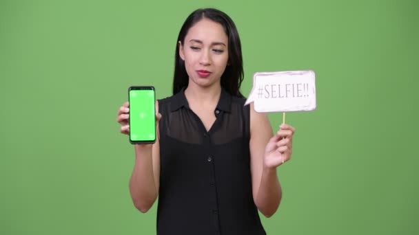 Молодая красивая азиатская бизнесвумен держит телефон и селфи бумажный знак — стоковое видео