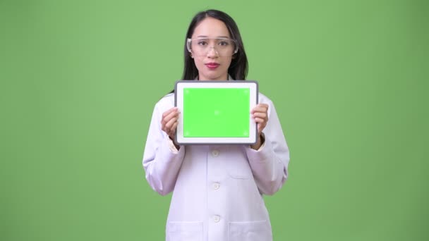 Joven hermosa mujer asiática médico usando gafas protectoras y mostrando tableta digital — Vídeo de stock