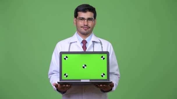 Joven guapo persa hombre médico mostrando portátil — Vídeo de stock