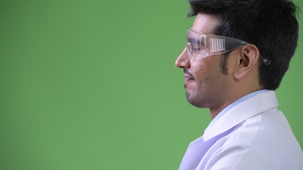 Vista del perfil del joven guapo médico persa con gafas protectoras pensando — Vídeos de Stock