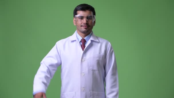 Joven guapo médico persa con gafas protectoras apuntando hacia arriba — Vídeos de Stock