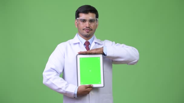 Jeune bel homme persan médecin portant des lunettes de protection montrant tablette numérique — Video