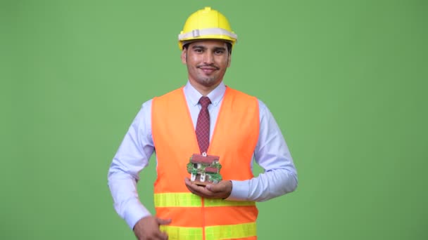 Joven hombre persa guapo trabajador de la construcción que sostiene la figura de la casa — Vídeos de Stock