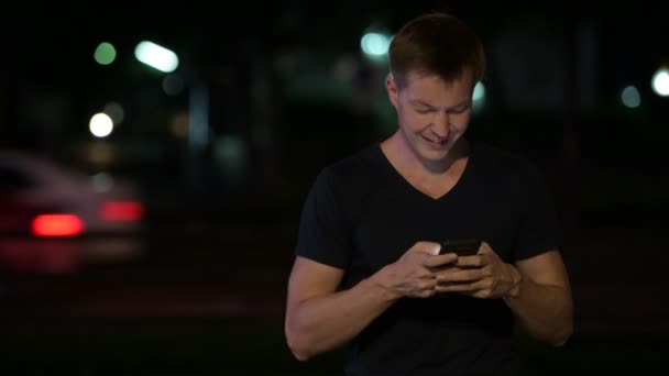 Mladý pohledný muž skandinávské pomocí telefonu v ulicích v noci — Stock video