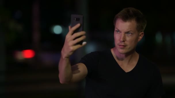 Jonge knappe Scandinavische man die lacht terwijl het nemen van een selfie buitenshuis in de nacht — Stockvideo