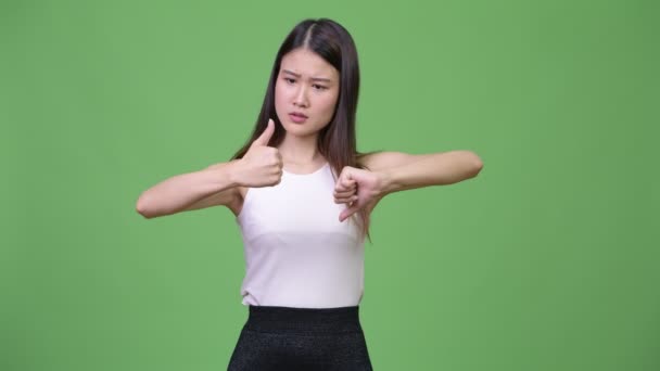Young confused Asian businesswoman choosing between thumbs up and thumbs down — Stock Video