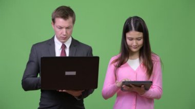 Genç Asyalı kadın ve genç işadamı dizüstü bilgisayar ve dijital tablet birlikte kullanma