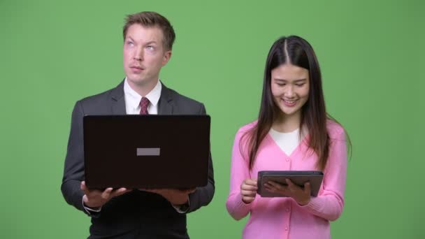 Joven mujer asiática y joven hombre de negocios utilizando ordenador portátil y tableta digital juntos — Vídeo de stock