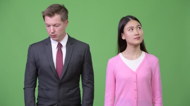 Young happy Asian woman and young sad businessman thinking together — Stock Video