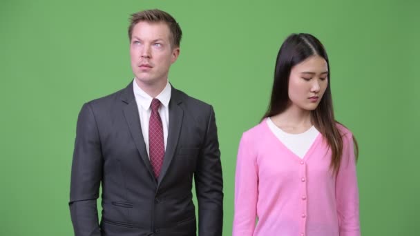 Молодая грустная азиатка и молодой счастливый бизнесмен думают вместе — стоковое видео