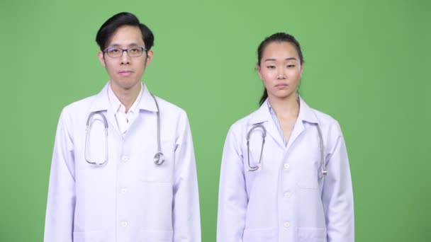 Jovens asiáticos casal médicos dando polegares para baixo juntos — Vídeo de Stock