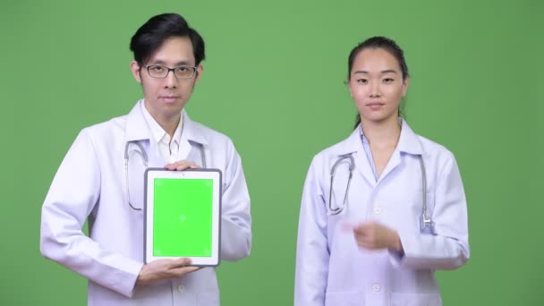 Jovens asiáticos casal médicos mostrando tablet digital juntos — Vídeo de Stock