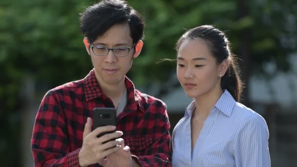 Jovem casal asiático usando telefone juntos ao ar livre — Vídeo de Stock