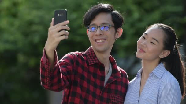 Fiatal ázsiai pár video hívás együtt szabadban — Stock videók