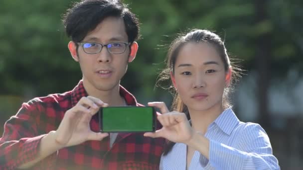 Jeune couple asiatique montrant téléphone ensemble à l'extérieur — Video