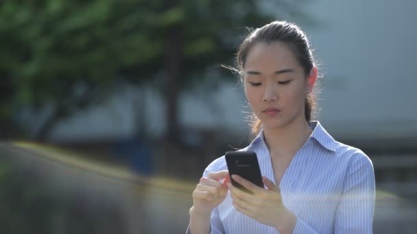 Unga glada vackra asiatiska affärskvinna använder telefonen utomhus — Stockvideo