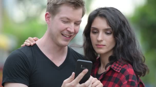 Jeune couple utilisant le téléphone ensemble à l'extérieur — Video