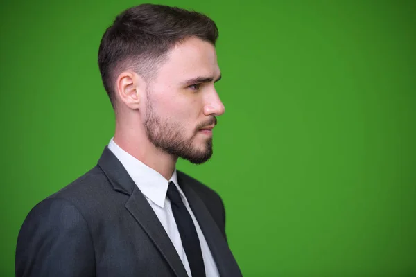 Jonge knappe bebaarde zakenman tegen groene achtergrond — Stockfoto