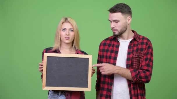 Молодая пара держит доску и указывает пальцем друг на друга — стоковое видео