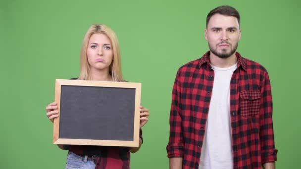 Fiatal pár, gazdaság, táblát ad hüvelykujját lefelé együtt — Stock videók