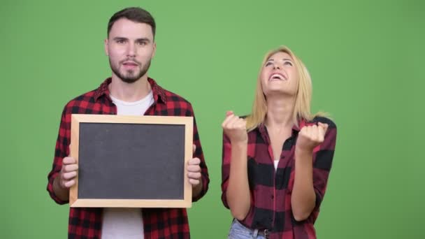 Holding blackboard ve birlikte heyecan arayan genç çift — Stok video
