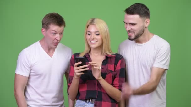 Trois jeunes amis heureux utilisant le téléphone ensemble et regardant excité — Video