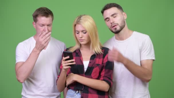 Tres jóvenes amigos usando el teléfono juntos y recibiendo malas noticias — Vídeos de Stock