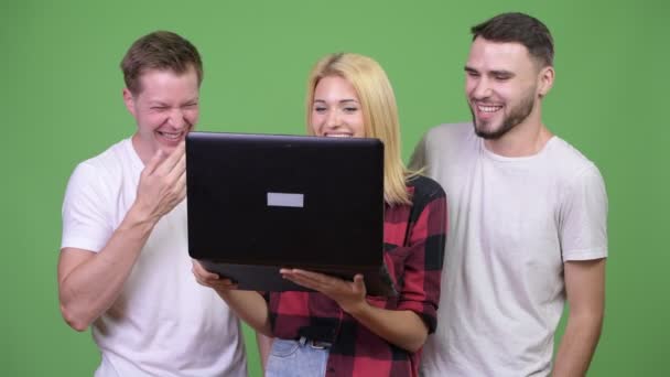 Tres felices jóvenes amigos sonriendo mientras usan el ordenador portátil juntos — Vídeos de Stock