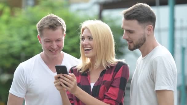 Tres jóvenes amigos felices sonriendo mientras usan el teléfono juntos en las calles al aire libre — Vídeo de stock