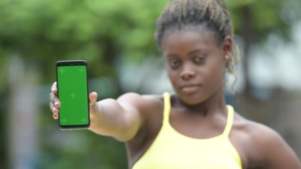 Unga glada afrikanska kvinnan visar telefonen utomhus — Stockvideo