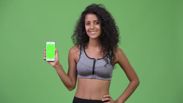 Jeune belle femme hispanique avec des vêtements de gym montrant téléphone — Video