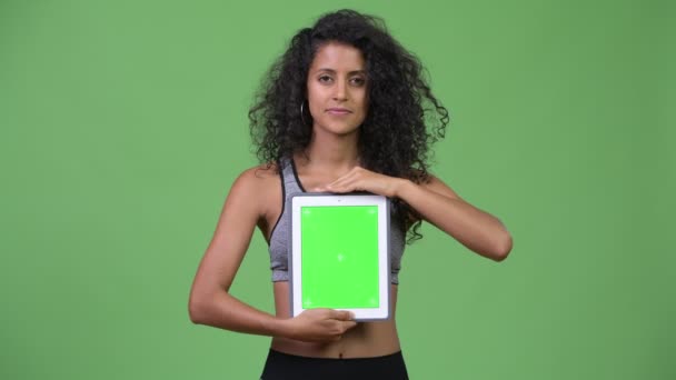 Νεαρή όμορφη γυναίκα Ισπανόφωνος με ρούχα γυμναστικής δείχνει ψηφιακή δισκίο — Αρχείο Βίντεο