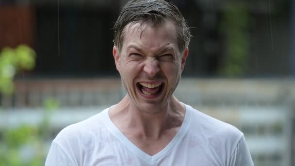 Человек на улице под дождем смеется и выглядит сумасшедшим — стоковое видео