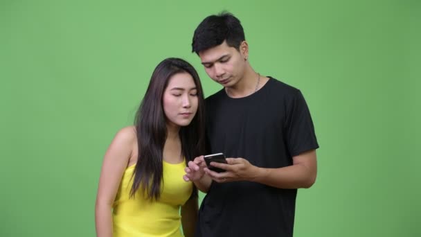 Молодая азиатская пара, пользующаяся телефоном и выглядящая потрясенной вместе — стоковое видео