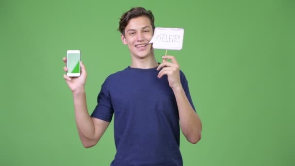 Jonge knappe tiener telefoon en selfie papier teken tonen — Stockvideo