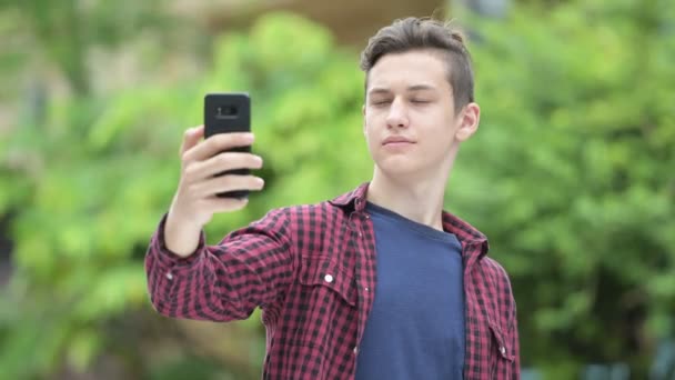 Unga glada tonårspojke tar selfie utomhus — Stockvideo