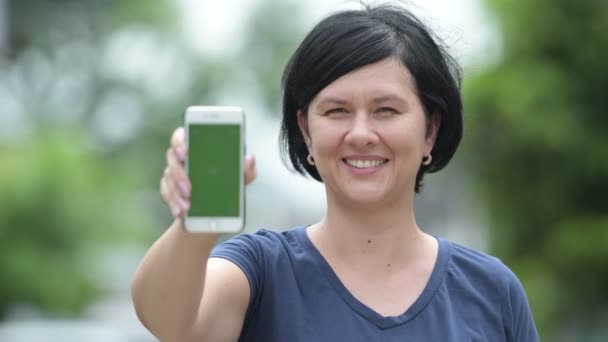 Feliz hermosa mujer mostrando el teléfono al aire libre — Vídeos de Stock