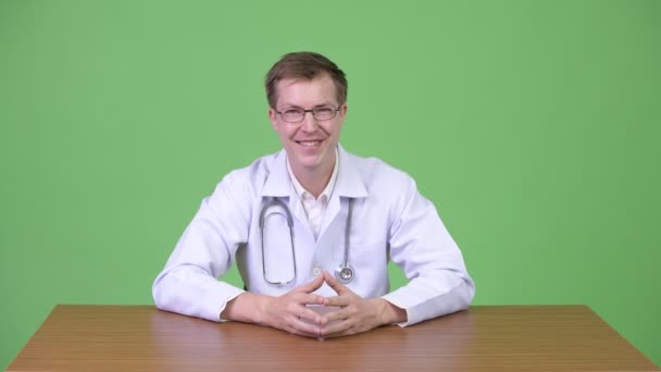 笑みを浮かべて、指を上向きながら座っている幸せな男医師 — ストック動画