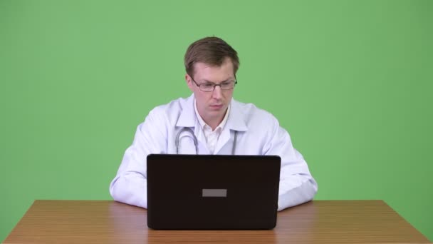 Homem médico sentado e usando computador portátil enquanto fala e cumprimenta paciente — Vídeo de Stock