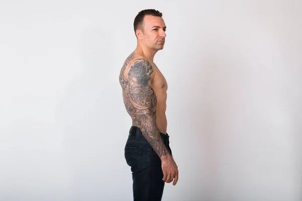 Vista del perfil del hombre sin camisa con tatuajes contra fondo blanco — Foto de Stock
