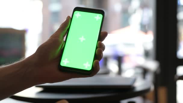 Nahaufnahme der Hand eines Mannes mit Handy mit grünem Bildschirm in Restaurant