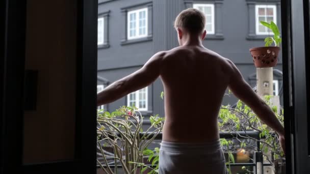 Hemdloser Mann öffnet Tür und geht auf Balkon ins Freie — Stockvideo