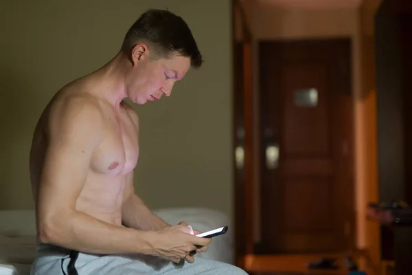 Uomo senza maglietta che utilizza il telefono cellulare di notte a letto — Foto Stock