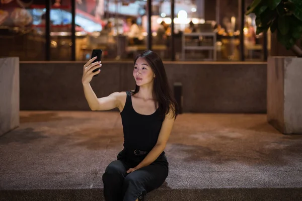Hermosa mujer asiática al aire libre en la noche tomando selfie con teléfono móvil — Foto de Stock