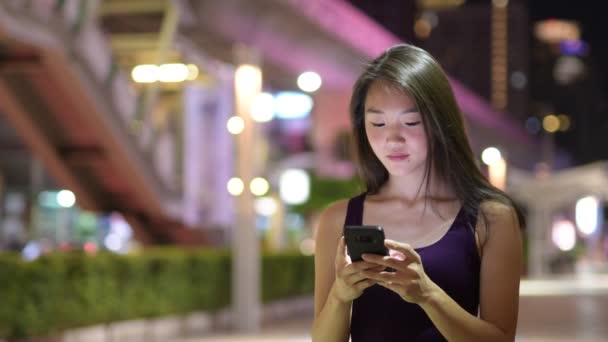 Hermosa mujer asiática al aire libre en la noche usando el teléfono móvil — Vídeos de Stock