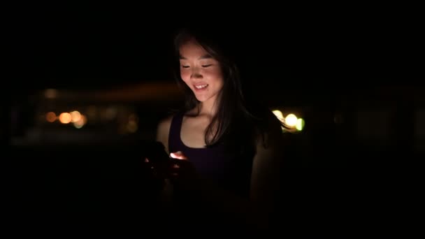 Hermosa mujer asiática al aire libre en la noche usando el teléfono móvil — Vídeos de Stock