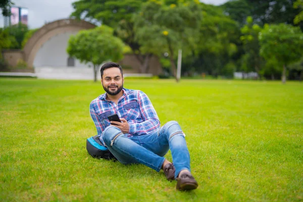 Bel homme indien dans le parc couché sur l'herbe et tenant téléphone portable — Photo