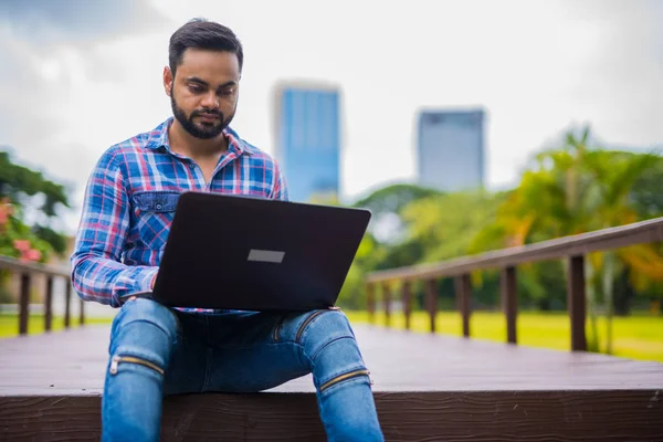 Joven guapo indio hombre en el parque usando ordenador portátil — Foto de Stock