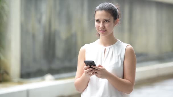 Portret pięknej młodej kobiety szczęśliwy na zewnątrz przy użyciu telefonu komórkowego — Wideo stockowe