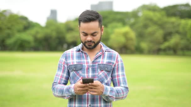Mladý pohledný indický muž v parku pomocí mobilního telefonu — Stock video